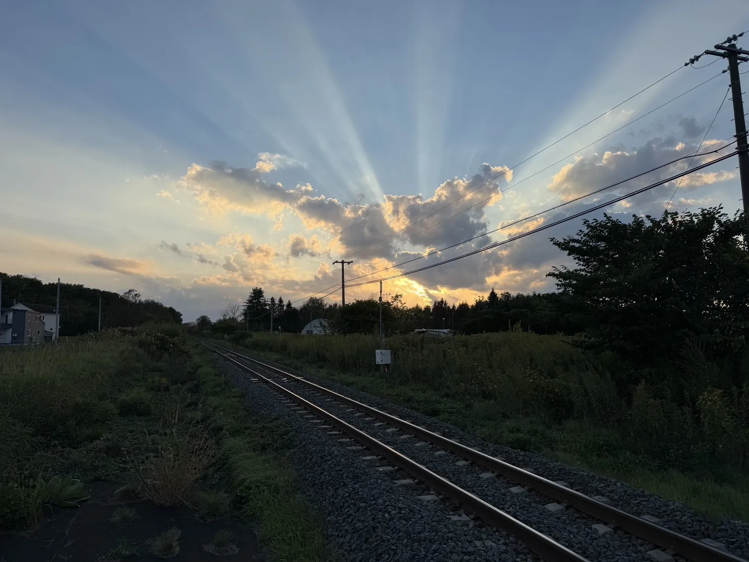 線路の先、雲間から光芒がのびる夕日